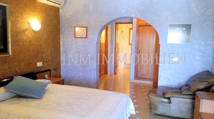 Dormitorio luminoso con cama doble, sillón de cuero, aire acondicionado y elegante paso de arco de medio punto en Santa Ponsa.