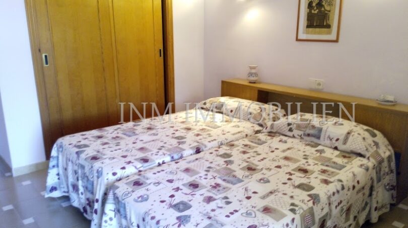 Dormitorio luminoso con cama doble, ropa de cama estampada, armario de madera y lámpara de pared en casa unifamiliar Santa Ponsa