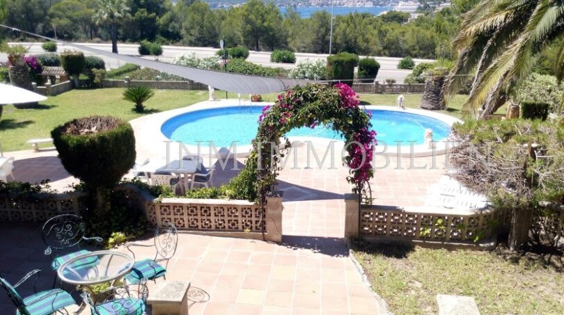 Área exterior con piscina ovalada, arco de flores, terraza y vista al mar de la casa unifamiliar en Santa Ponsa