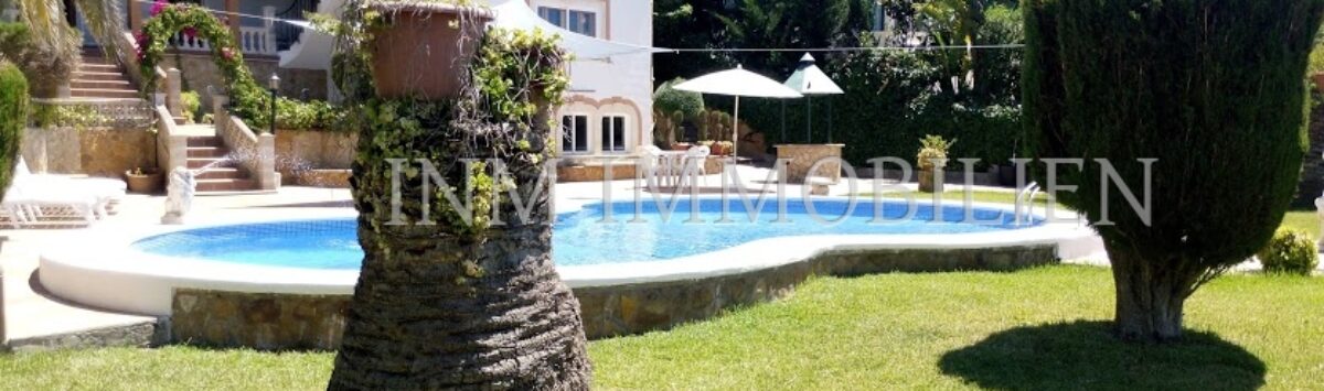 Vista exterior villa Santa Ponsa: Jardín bien cuidado con piscina, palmera y arquitectura mediterránea bajo el sol.