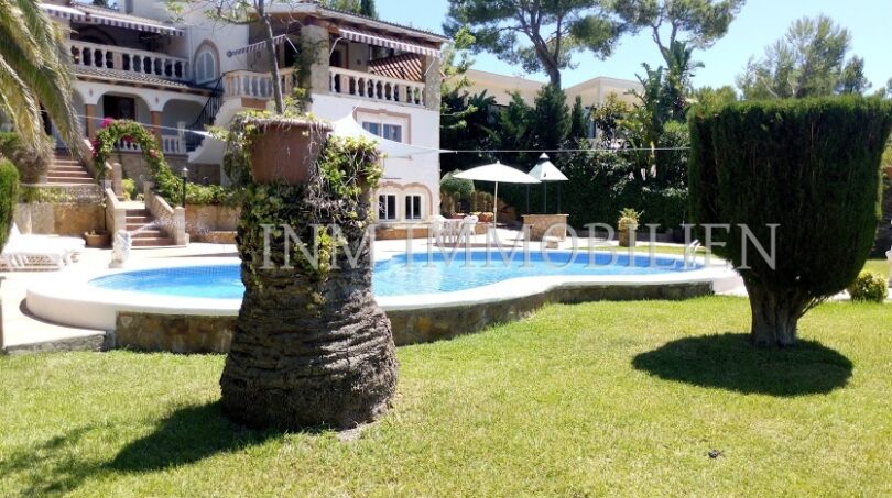 Vista exterior villa Santa Ponsa: Jardín bien cuidado con piscina, palmera y arquitectura mediterránea bajo el sol.
