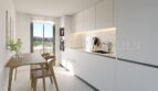 Moderna cocina blanca integrada con mesa de comedor y acceso al balcón en el apartamento áticos de nueva construcción en Palmanova