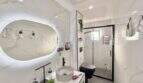 Modernes Badezimmer mit Marmoroptik, Aufsatzwaschbecken, beleuchtetem Spiegel und Glasdusche in Maisonette Porto Cristo