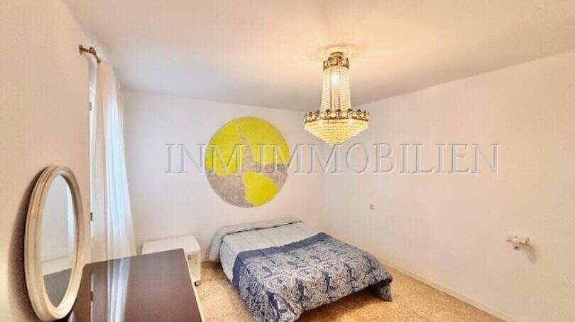 Helles Schlafzimmer der Stranwohnung in El Arenal mit Doppelbett, Kristallleuchter und rundem Wandbild.
