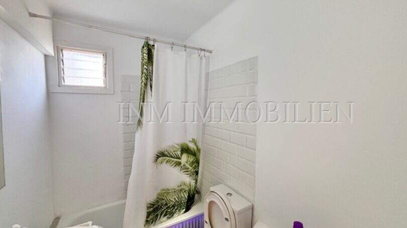 Helles Badezimmer der Strandwohnung in El Arenal mit Badewanne, Duschvorhang und kleinem Fenster.