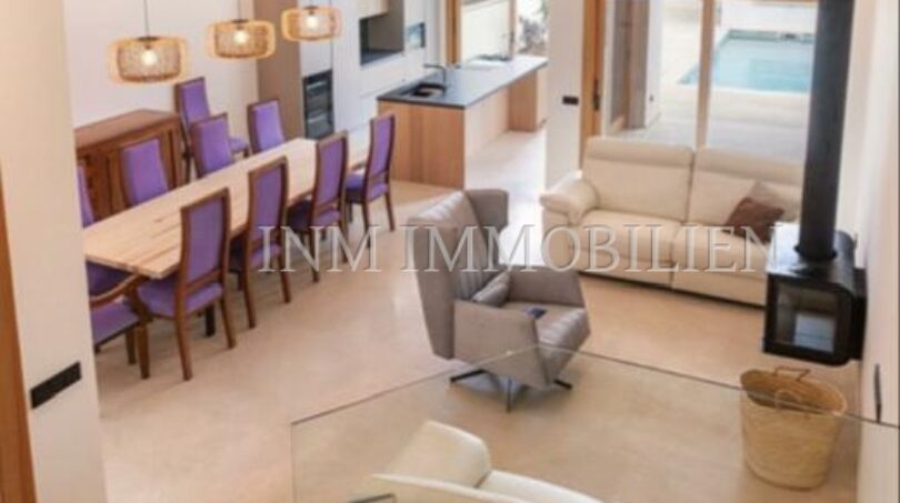 Open living-dining area with purple chairs, fireplace and pool view in luxury new build in Biniali