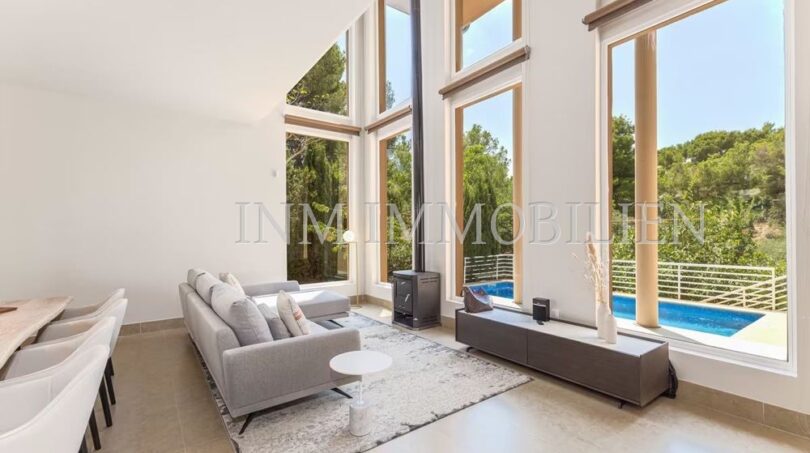 Bright living room with panoramic windows, fireplace and pool view of the villa in Cala Vinyes