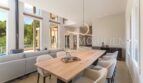 Light-filled dining area with large wooden table, modern chairs and panoramic windows to the pool area of the villa in Cala Vinyes.