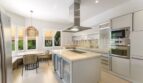 Modern fitted kitchen with kitchen island, stainless steel extractor hood and dining area in Villa Cala Vinyes