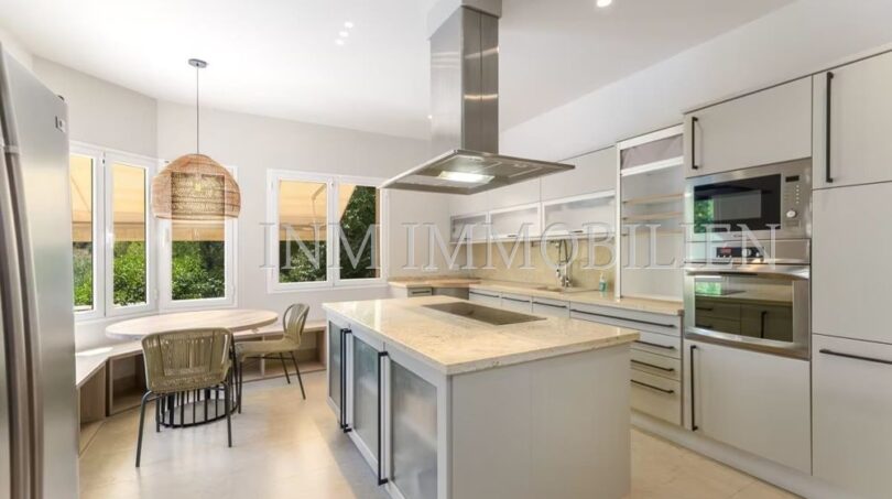 Modern fitted kitchen with kitchen island, stainless steel extractor hood and dining area in Villa Cala Vinyes
