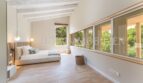 Bright bedroom of the villa in Cala Vinyes with wooden ceiling, parquet floor and panoramic window to the greenery.