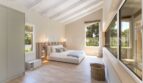 Bright bedroom of the villa in Cala Vinyes with wooden beam ceiling, parquet floor and large windows to the garden.