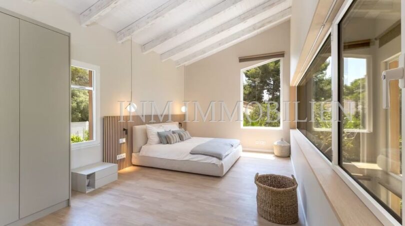 Bright bedroom of the villa in Cala Vinyes with wooden beam ceiling, parquet floor and large windows to the garden.