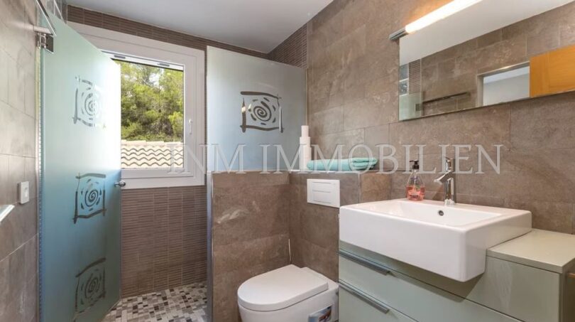 Modern bathroom of the villa in Cala Vinyes with shower, toilet and sink, brown natural stone look tiles