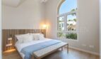 Bright bedroom of the villa in Cala Vinyes with double bed, wooden floor and large arched window to the garden.