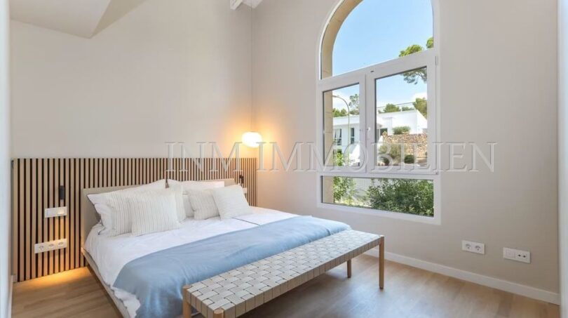 Bright bedroom of the villa in Cala Vinyes with double bed, wooden floor and large arched window to the garden.
