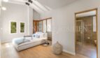 Bright bedroom with wooden floor, roof beams and en-suite bathroom of the villa in Cala Vinyes, Calvià.