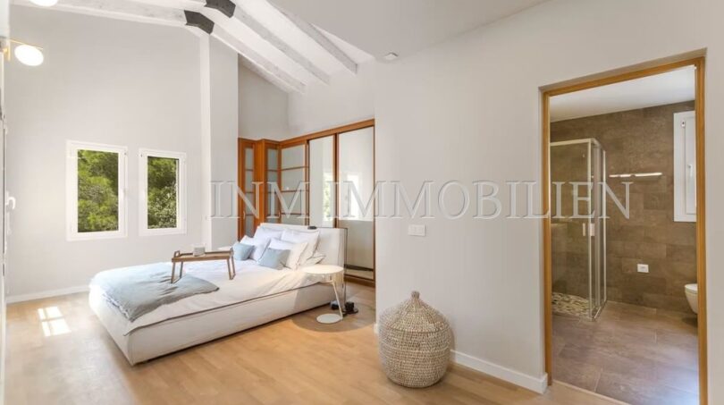Bright bedroom with wooden floor, roof beams and en-suite bathroom of the villa in Cala Vinyes, Calvià.