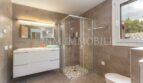 Modern bathroom of the villa in Cala Vinyes with glass shower, white sink and natural stone look tiles.