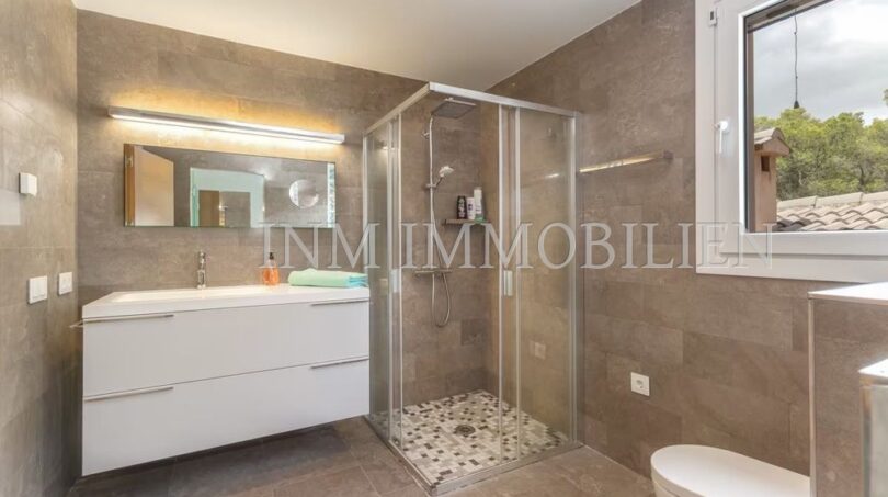 Modern bathroom of the villa in Cala Vinyes with glass shower, white sink and natural stone look tiles.