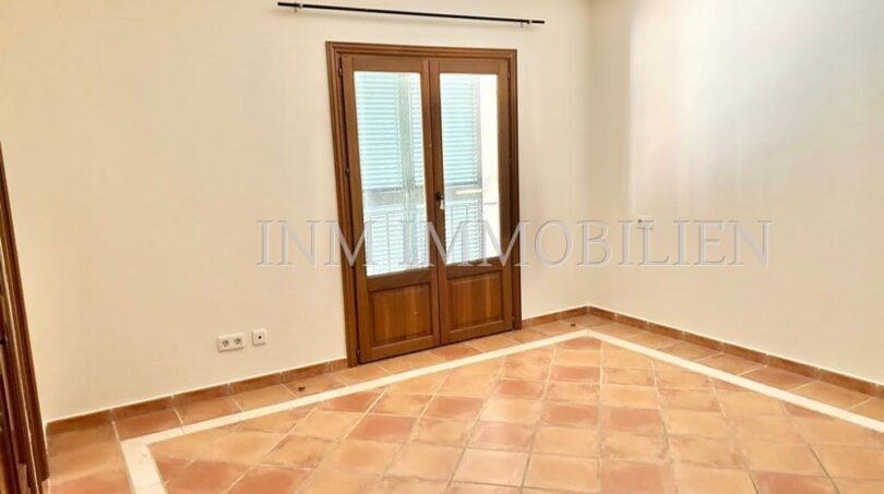 Habitación luminosa y vacía con azulejos de terracota y puerta de madera de dos hojas a la terraza en la finca Santanyí