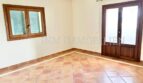 Habitación luminosa y vacía con suelo de terracota, ventana de madera y puerta de terraza en la finca Santanyí