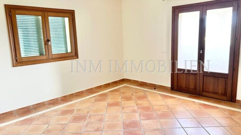 Habitación luminosa y vacía con suelo de terracota, ventana de madera y puerta de terraza en la finca Santanyí