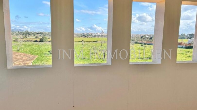 Habitación luminosa con cuatro grandes ventanas, vista a campos verdes y pueblo de Santanyí, finca Mallorca