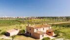 Vista aérea de una finca tradicional en Santanyí con edificio anexo, rodeada de campos verdes y cielo azul.