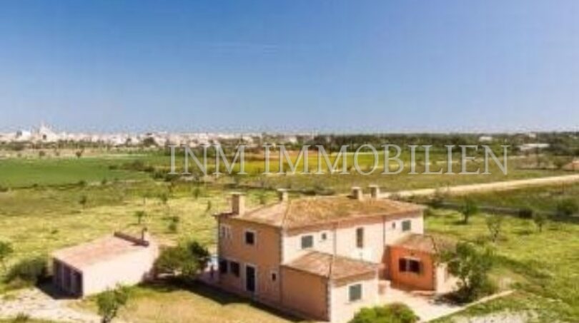 Vista aérea de una finca tradicional en Santanyí con edificio anexo, rodeada de campos verdes y cielo azul.