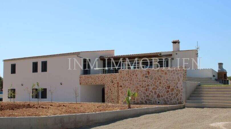 Exterior view of a high-quality finca in Campos with natural stone wall, white façade, terrace and external stairs.