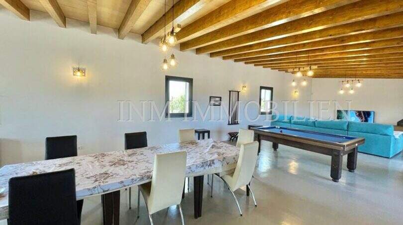 Spacious living room of the Campos finca with wooden beam ceiling, dining table, pool table and turquoise sofa.