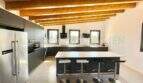 Modern kitchen of the Campos finca with kitchen island, bar stools, stainless steel refrigerator and rustic wooden ceiling beams.