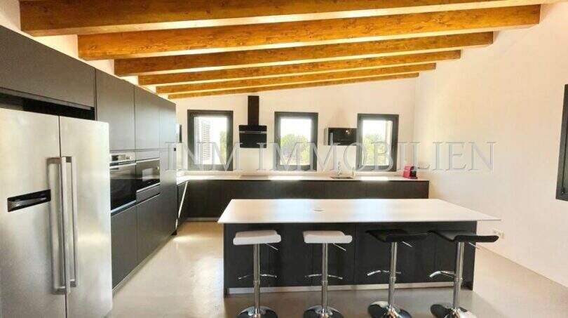 Modern kitchen of the Campos finca with kitchen island, bar stools, stainless steel refrigerator and rustic wooden ceiling beams.