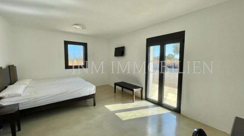Bright bedroom of the Campos finca with double bed, TV, terrace access and modern concrete flooring.