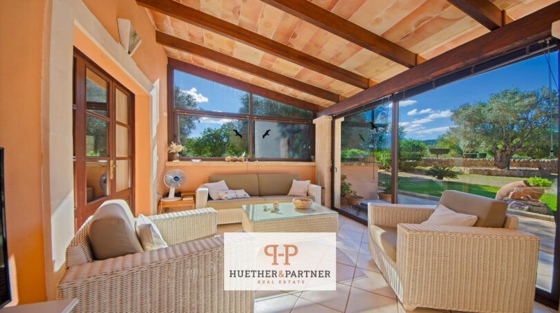 Terraza cubierta de la finca Felanitx con muebles de ratán, techo de vigas de madera y vistas al jardín verde
