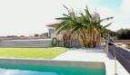 Outdoor pool with turquoise water, lawn area and palm tree in front of modern finca in Campos, Mallorca