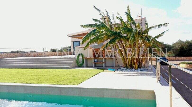 Outdoor pool with turquoise water, lawn area and palm tree in front of modern finca in Campos, Mallorca