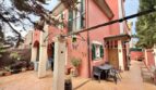 Außenansicht: Gepflegtes rotes Reiheneckhaus mit überdachter Terrasse, Gartenmöbeln und Bepflanzung in Pollença.