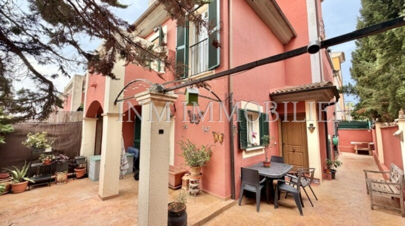Außenansicht: Gepflegtes rotes Reiheneckhaus mit überdachter Terrasse, Gartenmöbeln und Bepflanzung in Pollença.