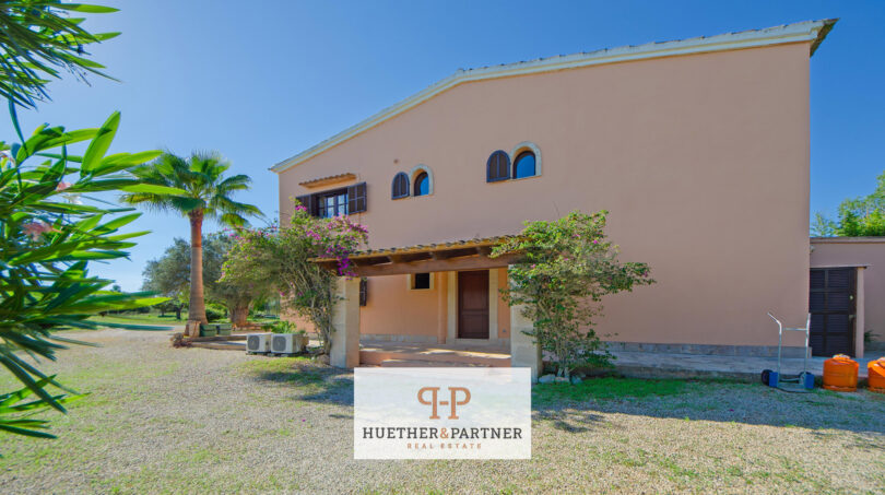 Vista exterior de la finca en Felanitx con fachada rosa, pérgola, palmeras y jardín de grava bien mantenido