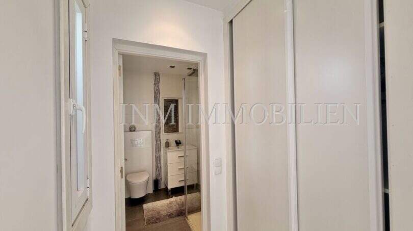 Heller Flur mit Schiebetür, Blick ins moderne Bad mit WC, Dusche und Waschtisch im Penthouse Cala Pi.