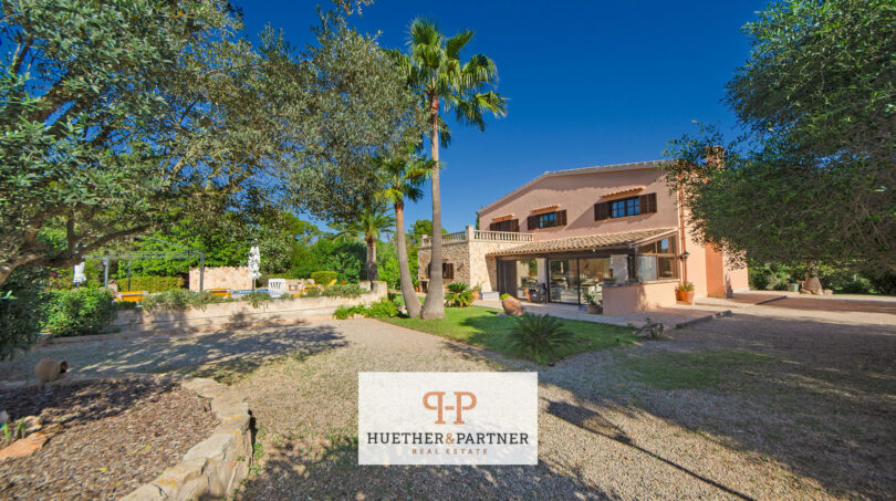 Vista exterior de la finca Felanitx con palmeras, jardín mediterráneo, muros de piedra natural y piscina al fondo.