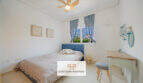 Helles Schlafzimmer mit blauem Bettrahmen, Deckenventilator und Holzschreibtisch im Haus Cala Murada