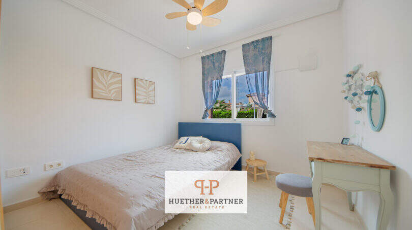 Helles Schlafzimmer mit blauem Bettrahmen, Deckenventilator und Holzschreibtisch im Haus Cala Murada