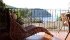 Sonnige Terrasse mit Rattanliege und Meerblick auf die Bucht von Port de Sóller, umrahmt von Pinien