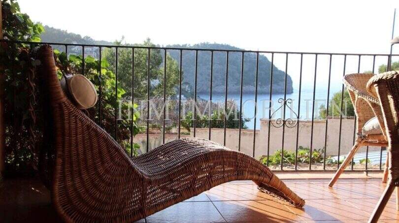Sonnige Terrasse mit Rattanliege und Meerblick auf die Bucht von Port de Sóller, umrahmt von Pinien