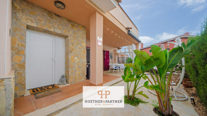 Eingangsbereich eines Hauses in Cala Murada mit Natursteinwand, Garage und überdachter Terrasse mit Garten.