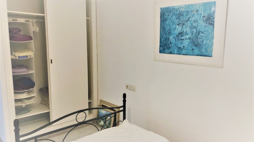 Helles Schlafzimmer der Mietwohnung in Cala Ratjada mit Doppelbett, Einbauschrank und blauem Kunstwerk.