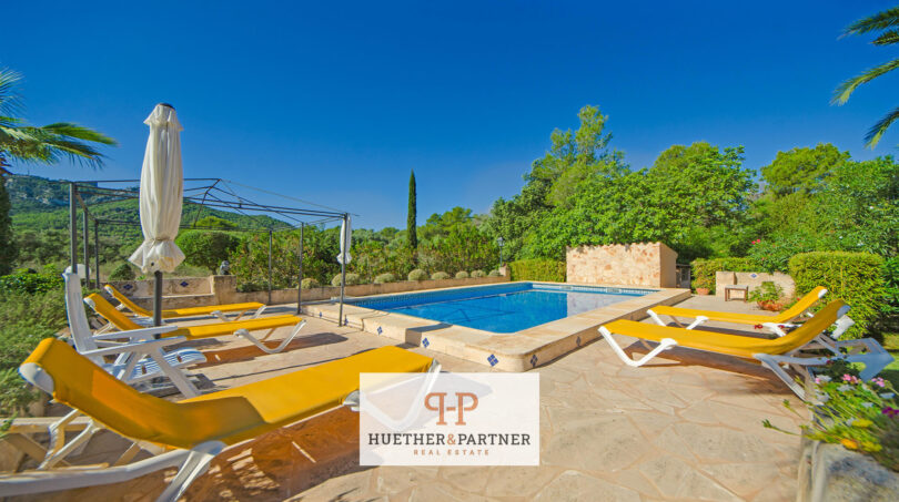 Zona de piscina de la finca Felanitx con tumbonas amarillas, sombrilla y vistas a montañas boscosas